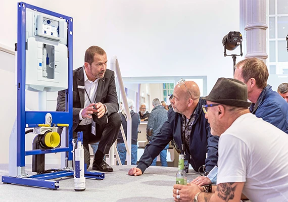  A sales associate is presenting a plumbing system to a group of listeners at a fair