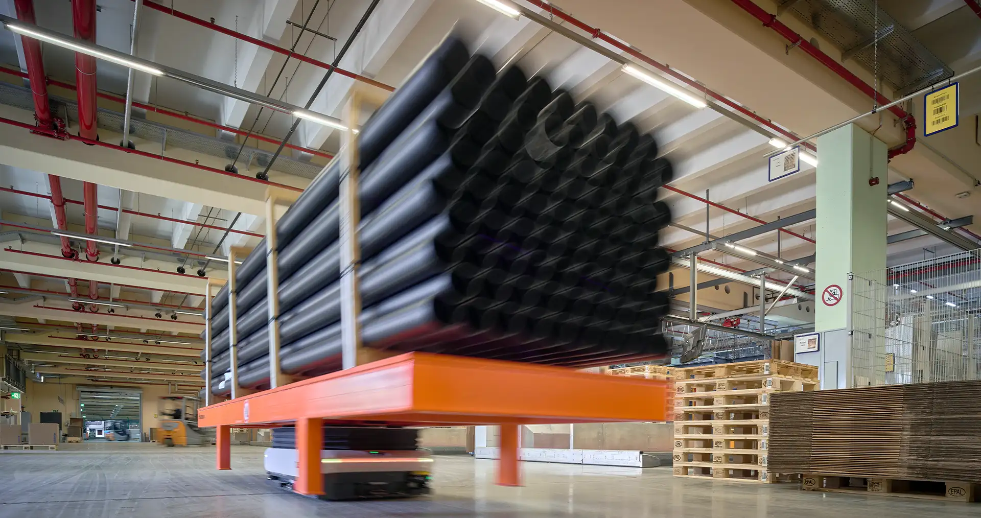 Automated transport system moves large black pipes in an industrial warehouse