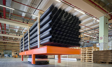 Automated transport system moves large black pipes in an industrial warehouse