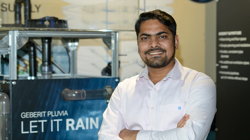 Smiling Vineet Kumar Bhaskar with crossed arms standing in front of a Geberit Pluvia