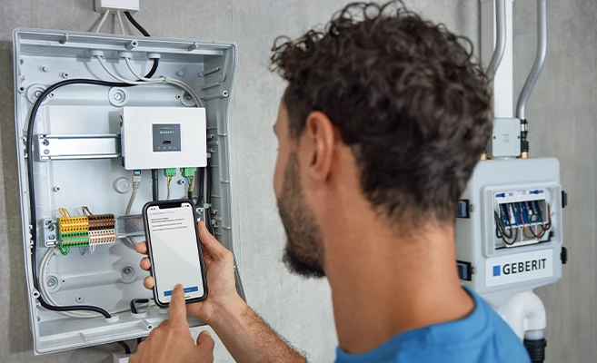 Technician uses smartphone to control and monitor sanitary appliances with Geberit Connect technology in a modern bathroom