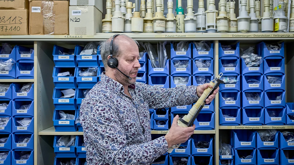 Olaf Schütter in front of a shelf with flush valve models and spare parts