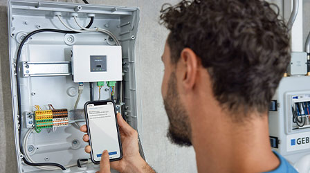 Technician uses smartphone to control and monitor sanitary appliances with Geberit Connect technology in a modern bathroom