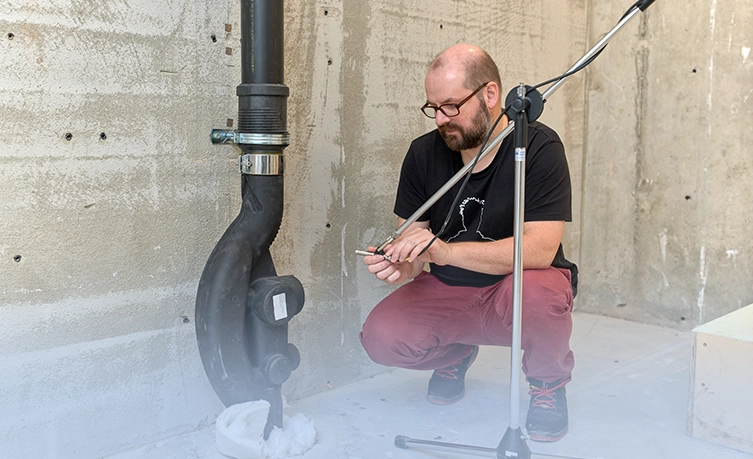A man wearing glasses kneeling and preparing a measurement in the Technology and Acoustics Laboratory in Rapperswil-Jona (CH). (Photo)