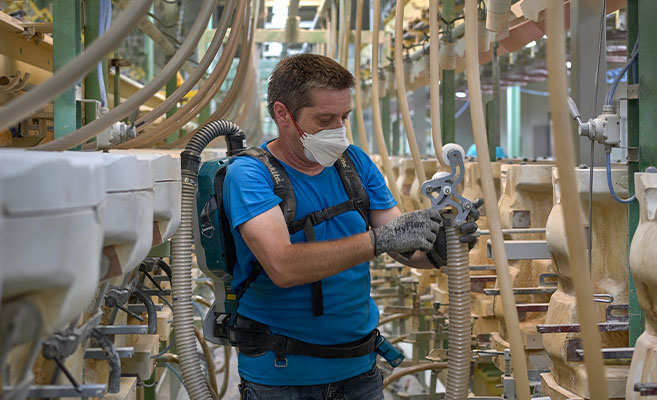Ein Mitarbeiter saugt in einer Produktionsanlage den Staub aus den Schläuchen ab 