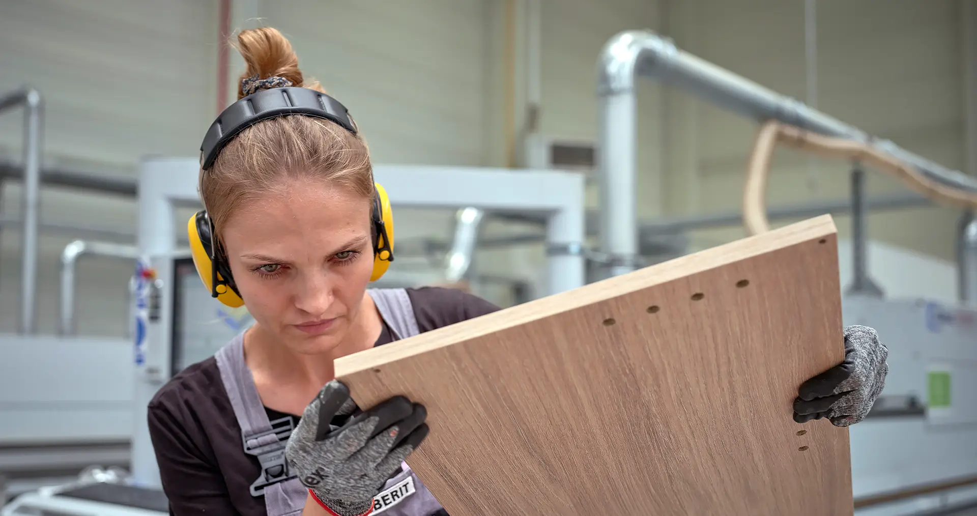 Arbeiterin überprüft sorgfältig ein Holzbrett in einer modernen Möbelfabrik