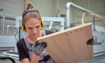 Arbeiterin überprüft sorgfältig ein Holzbrett in einer modernen Möbelfabrik