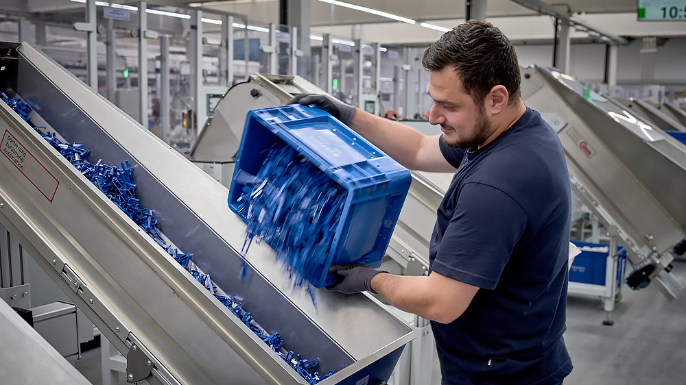 Co-operator Senol Yildiz füllt eine Produktionsanlage mit blauen Kunststoffteilen
