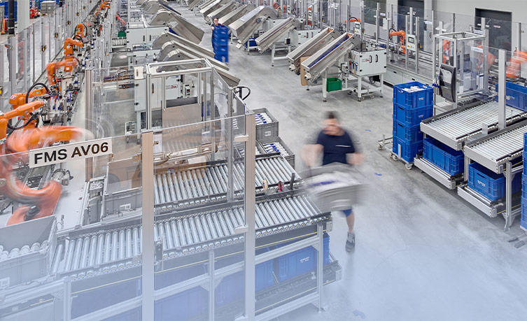 Moderne Fabrikhalle mit Robotern und Arbeitern, die Produktions- und Logistikprozesse durchführen