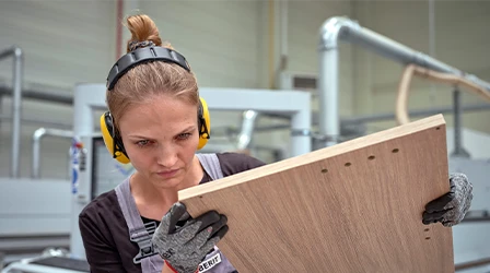 Arbeiterin überprüft sorgfältig ein Holzbrett in einer modernen Möbelfabrik